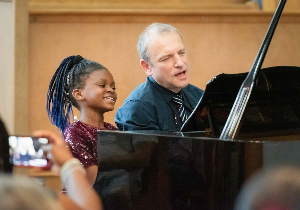 Black young piano girl student smiling while playing in duet with her teacher at Artgate event